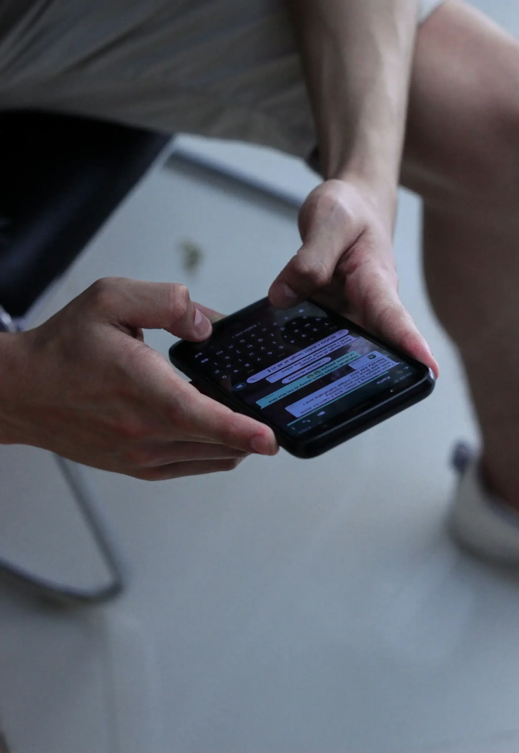 Um close-up das mãos de um homem segurando um smartphone e digitando em um aplicativo de mensagens.